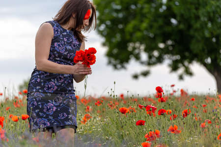 A young woman in a blue dress in a poppy flower field with beautiful clouds in the backgroundの写真素材