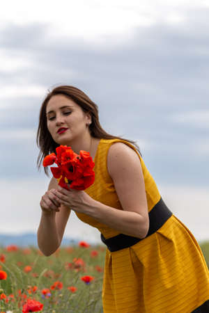 A young woman in a yellow dress in a poppy flower field with beautiful clouds in the backgroundの写真素材