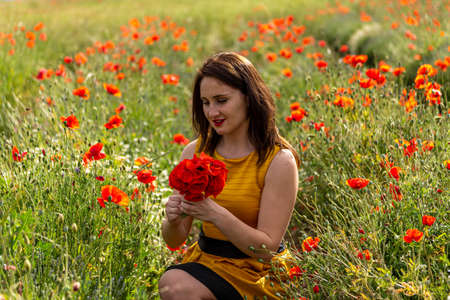 A young woman in a yellow dress in a poppy flower field with beautiful clouds in the backgroundの写真素材