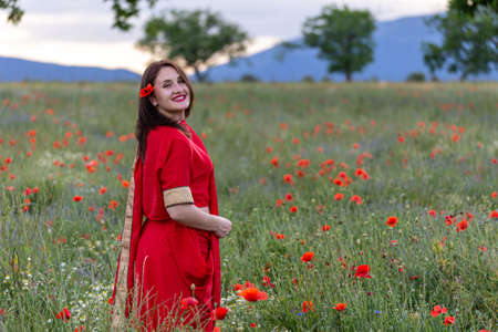 Young woman dressed in a traditional Indian costume called Sari walking in a red poppy flower fieldの写真素材