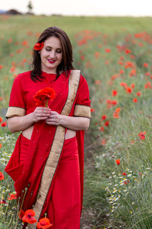 Young woman dressed in a traditional Indian costume called Sari walking in a red poppy flower fieldの写真素材