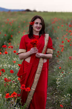 Young woman dressed in a traditional Indian costume called Sari walking in a red poppy flower fieldの写真素材