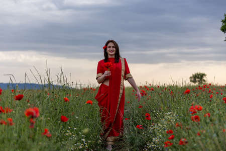 Young woman dressed in a traditional Indian costume called Sari walking in a red poppy flower fieldの写真素材