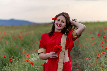 Young woman dressed in a traditional Indian costume called Sari walking in a red poppy flower fieldの写真素材