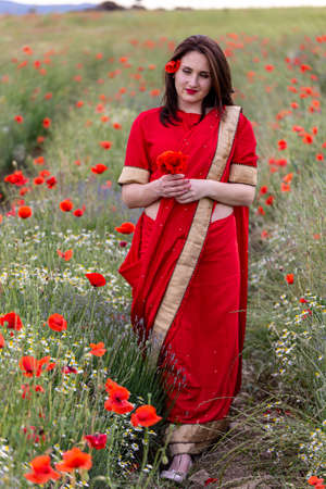 Young woman dressed in a traditional Indian costume called Sari walking in a red poppy flower fieldの写真素材