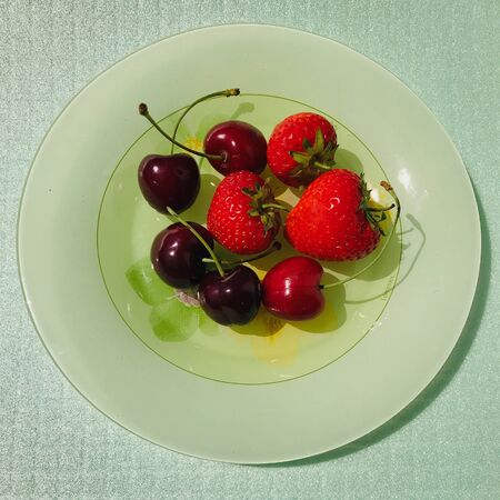 Cherries and strawberries over a green plate and on a light green backgroundの写真素材