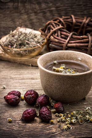 mug of tea and dried berries of the wild rose on wooden tableの写真素材