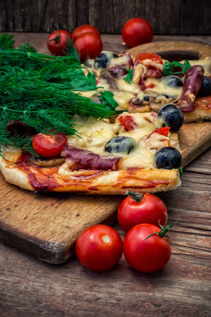 hunk of delicious meat pizza with bacon and olives on the background of the vegetables.の写真素材