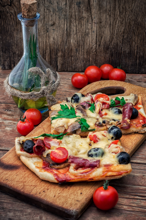 hunk of delicious meat pizza with bacon and olives on the background of the vegetables.The image is tintedの写真素材