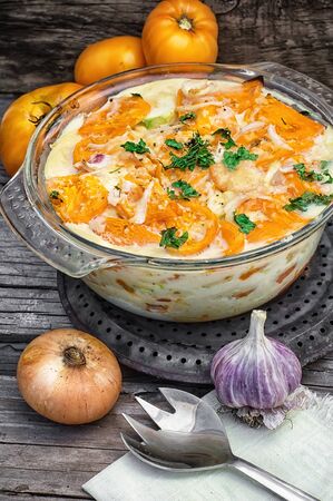 gratin of zucchini and yellow tomatoes on wooden background in glass bowlの写真素材