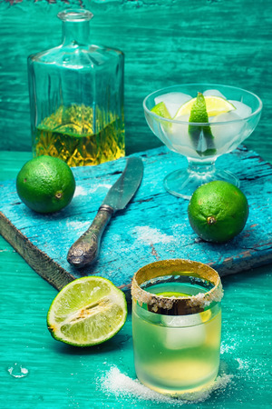 Glass with alcohol and fruits of lime and the bowl with ice  on wooden backgroundの写真素材