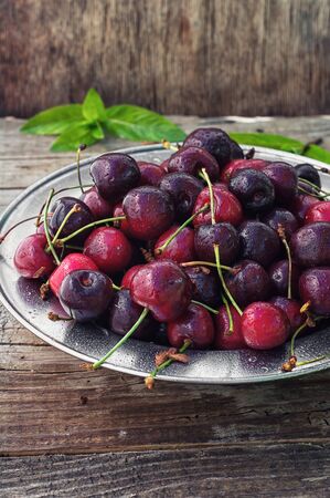 Ripe cherries on wooden background in the iron bowlの写真素材