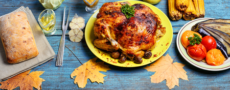 Kitchen table with baked chicken in vegetables and strewn with autumn leavesの写真素材