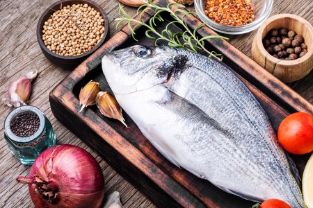 Fresh uncooked dorado fish with herbs and spices on rustic wooden board