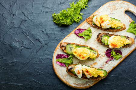 Bruschetta with poached egg, cucumber and fried mushrooms with hollandaise sauce. Tasty eggs benedictの写真素材