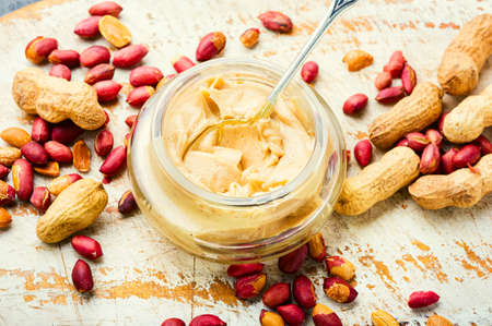 Peanut paste in glass jar. Peanut butter and heap of nuts