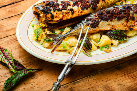 Delicious baked mackerel fish in a plate on wooden kitchen table. Roasted mackerel with boiled potatoesの写真素材
