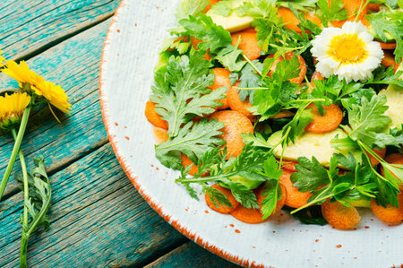 Diet salad with chrysanthemum leaves, carrots, avocado and greens. Vegetarian salad on rustic wooden background.の写真素材