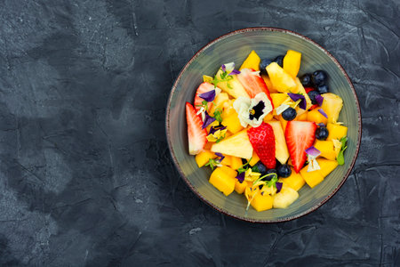 Salad of pineapple, strawberries and berries, decorated with edible flowers. Vegan food. Copy space.の写真素材