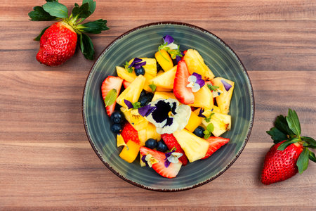 Colorful salad of pineapple, strawberries and berries, decorated with edible flowers in a bowlの写真素材