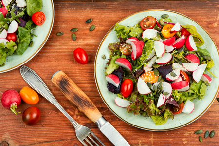 Dietary salad with radish, greens, tomato and sesame on old wooden table.の写真素材
