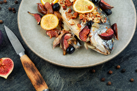 Fried dorado fish with garnish and figs on a black stone backgroundの写真素材