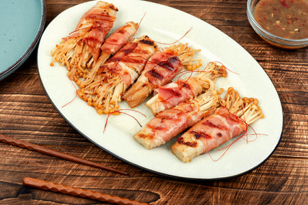 Enoki or enokitake mushroom roasted in bacon and sauce on wooden table.の写真素材
