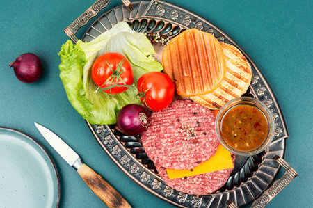 Raw burger patties, cheese, vegetables and burger buns for cooking. Raw steak cutlets with mince...