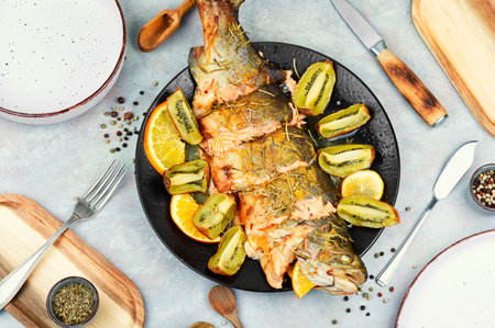 Plate of whole baked trout, served with kiwi fruit and orange.の写真素材
