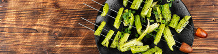 Roasted vegan skewers, celery kebabs on wooden rustic background. Plate of celery skewers, veggie style. Copy space. Space for text.の写真素材