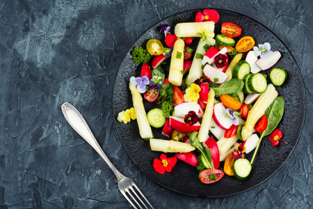 A juicy, green salad with white asparagus mixed vegetables arranged artfully on a plate, garnished with fresh herbs and edible flowers. Copy space.の写真素材