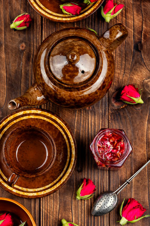 Delicious homemade rose jam in jar with rose flowers with tea utensils on wooden rustic background.の写真素材