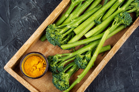Organic baby broccoli placed in a wooden tray with colorful spices on a concrete kitchen table