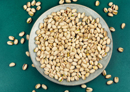 Salted pistachios served on a plate against a dark surface. Minimal food composition.