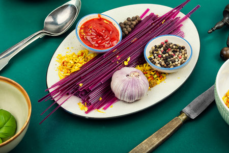 Uncooked vegetable pasta sticks made from purple sweet potato with spices and sauce on plate. Concept of homemade healthy alternative to traditional wheat pasta.の写真素材