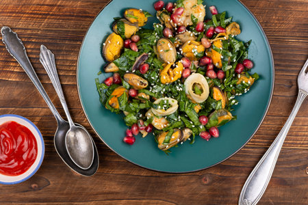 Nutritious salad combining fried shrimp, mussels and squid with leafy greens and pomegranate seeds on wooden surface.の写真素材
