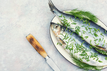 Whole salted herring garnished with fresh dill and chives on a ceramic plate. Copy space.