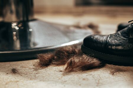 Cut brown hair is lying on the floor near the shoe and a metal barber chairの写真素材