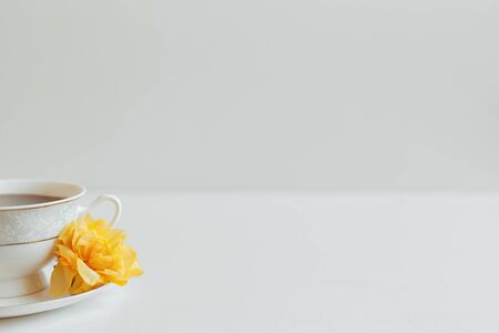 Cup of tea with a plate on a table with an orange flower on a white backgroundの写真素材