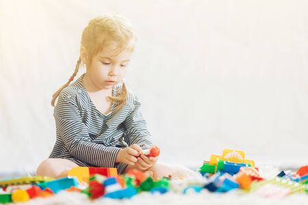 A little girl sits in a toy room on a white carpet and plays in a colored plastic constructorの写真素材