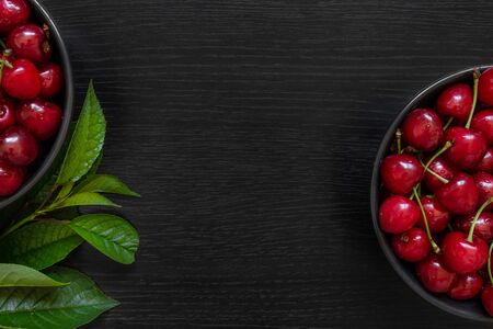 Red cherry with green leaves in a dark plate on a black table