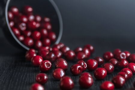 Ripe red cherry crumbles from a dark plate on a black table on a dark background close-up