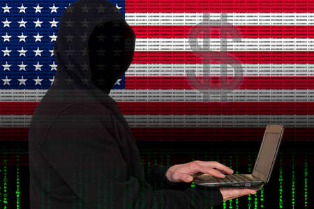 Hypothetical American hackers. An unknown person in a dark jacket with a hood holds a laptop in his...