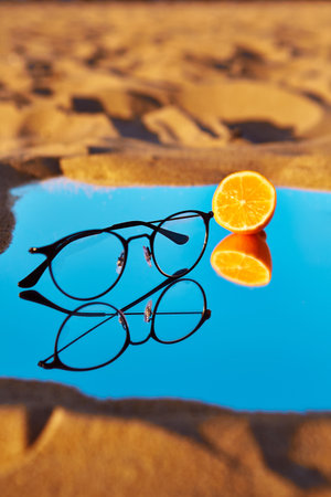 Close-up glasses lie on a mirror with an orange in the desertの写真素材
