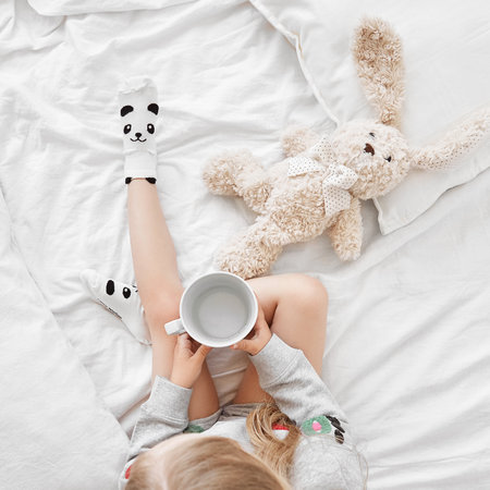 Top view of girl holding plush bunny toy sitting on bed wearing cute panda socksの写真素材