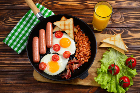 Full English breakfast with fried eggs, sausages, beans, toasts and juice on copy space background. On a wooden background.の写真素材