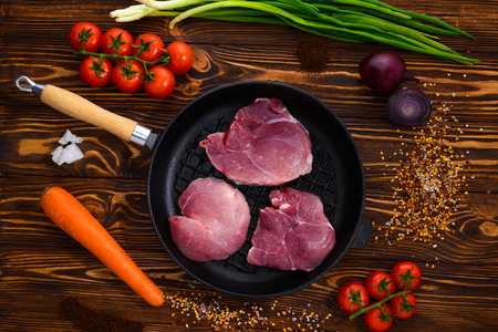 Raw pork steak in a frying pan with spices, cherry tomatoes, carrots, lettuce and onionsの写真素材