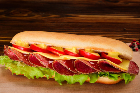 Sandwich with salami, cheese, cherry tomatoes, lettuce and mustard on a black background. Space for text or design.の写真素材