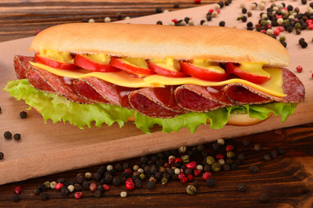 Sandwich with salami, cheese, cherry tomatoes, lettuce and mustard on a wooden table. の写真素材