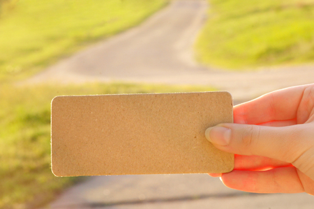 Girl holding empty card in a field with windmills and a road in sunny rays. Space for text.の写真素材